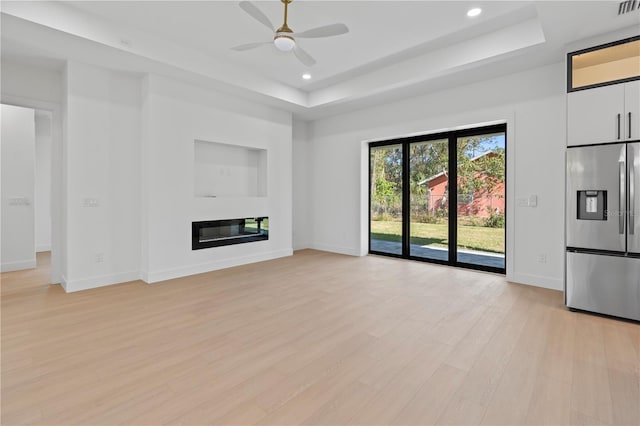 unfurnished living room with a raised ceiling, ceiling fan, and light hardwood / wood-style flooring