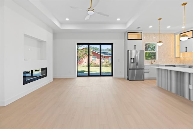 unfurnished living room featuring a raised ceiling, light hardwood / wood-style flooring, ceiling fan, and sink