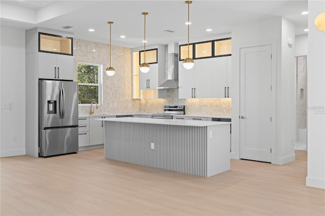 kitchen with a center island, wall chimney exhaust hood, stainless steel appliances, decorative light fixtures, and light wood-type flooring