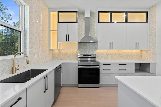 kitchen featuring white cabinets, wall chimney range hood, sink, appliances with stainless steel finishes, and light hardwood / wood-style floors