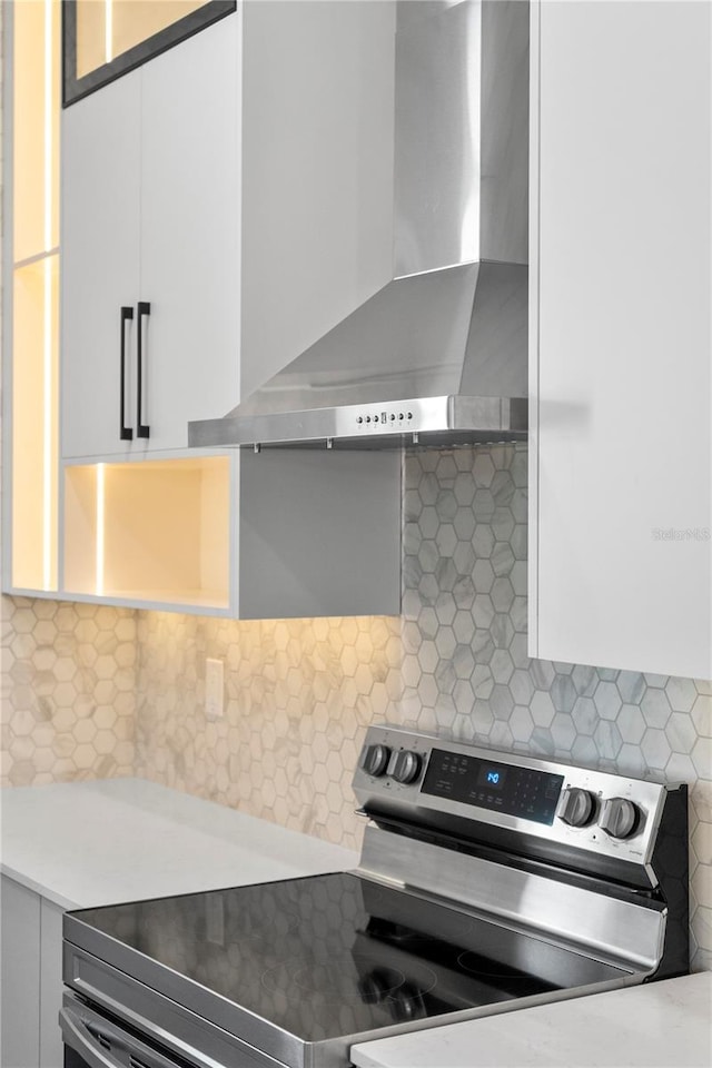 details with tasteful backsplash, white cabinetry, wall chimney exhaust hood, and stainless steel electric range