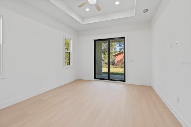 spare room featuring ceiling fan, a tray ceiling, and light hardwood / wood-style flooring