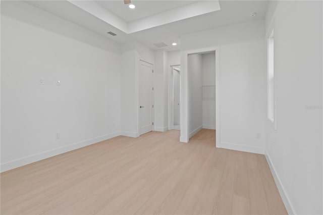 unfurnished bedroom featuring a tray ceiling, a spacious closet, a closet, and light wood-type flooring