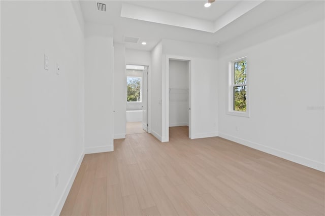 unfurnished bedroom with multiple windows, a spacious closet, a closet, and light wood-type flooring