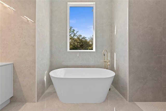 bathroom featuring tile patterned flooring, vanity, a tub, and tile walls