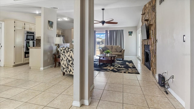 tiled living room featuring a stone fireplace, ceiling fan, and lofted ceiling