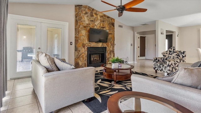 tiled living room featuring french doors, vaulted ceiling, ceiling fan, and a stone fireplace