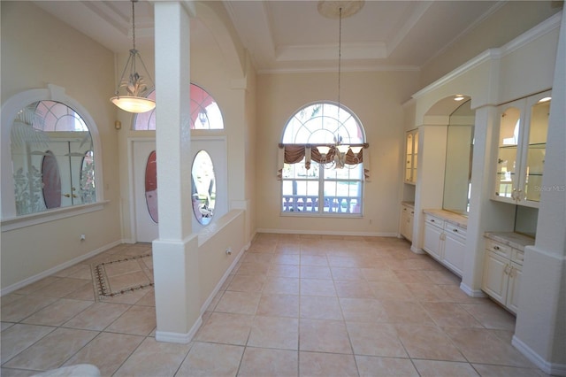 entryway featuring light tile patterned floors, a towering ceiling, a raised ceiling, and ornamental molding