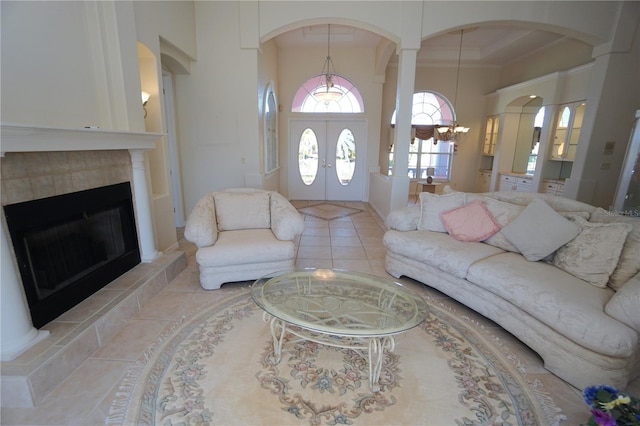 living room with french doors, a towering ceiling, a chandelier, a tiled fireplace, and light tile patterned floors