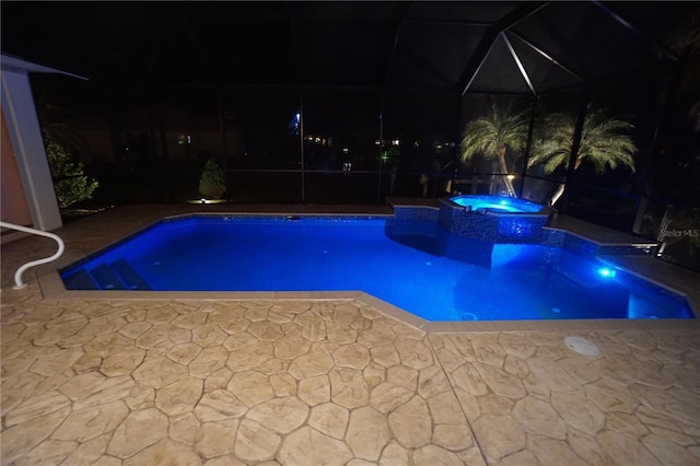 pool at night featuring a patio area, a lanai, and a pool with connected hot tub