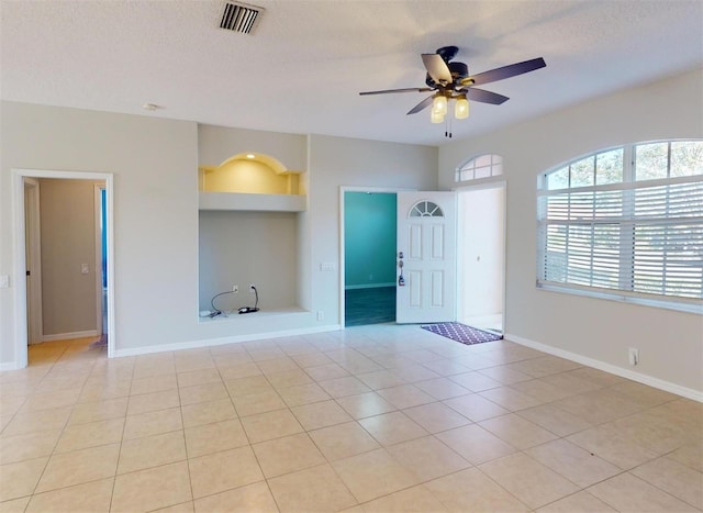 empty room featuring built in shelves, ceiling fan, light tile patterned floors, and a textured ceiling