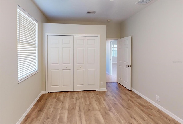 unfurnished bedroom with light wood-type flooring, multiple windows, and a closet