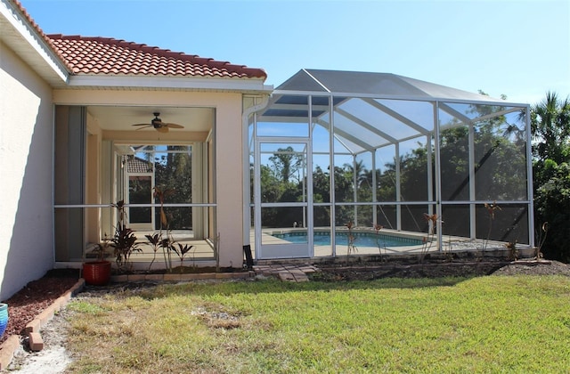 view of pool with glass enclosure, ceiling fan, and a lawn