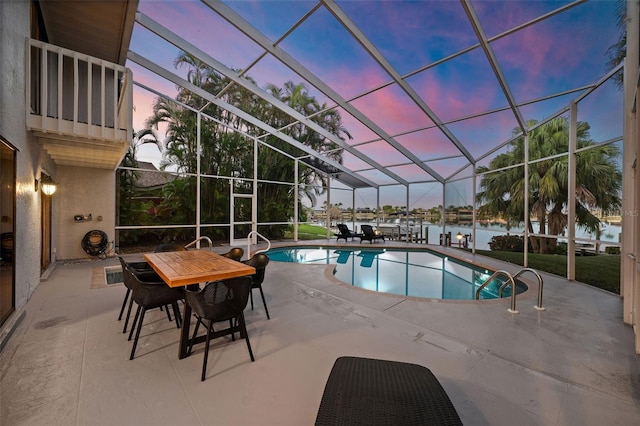 pool at dusk featuring a lanai, a water view, and a patio