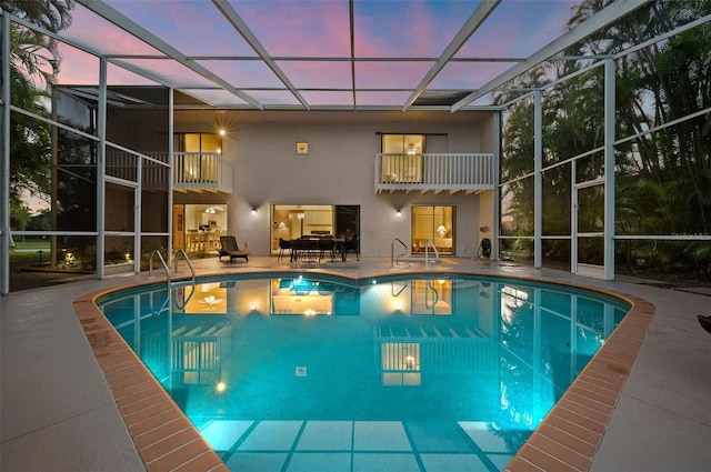 pool at dusk featuring glass enclosure and a patio area