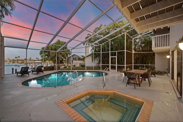 pool at dusk with glass enclosure, a water view, an in ground hot tub, and a patio