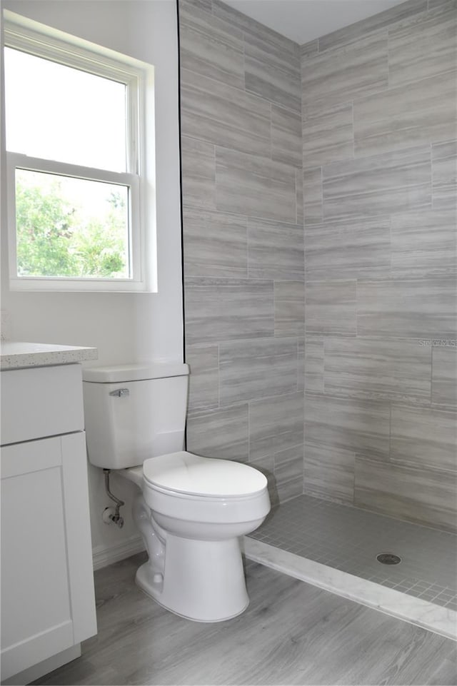 bathroom featuring a shower, toilet, vanity, tile walls, and hardwood / wood-style flooring