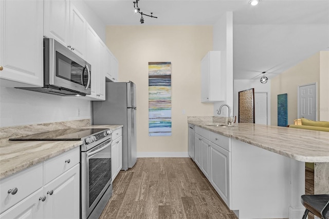 kitchen with white cabinets, appliances with stainless steel finishes, light hardwood / wood-style floors, kitchen peninsula, and a breakfast bar area