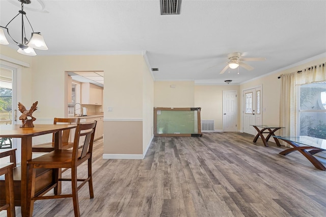 dining area with sink, light hardwood / wood-style floors, ceiling fan with notable chandelier, and ornamental molding