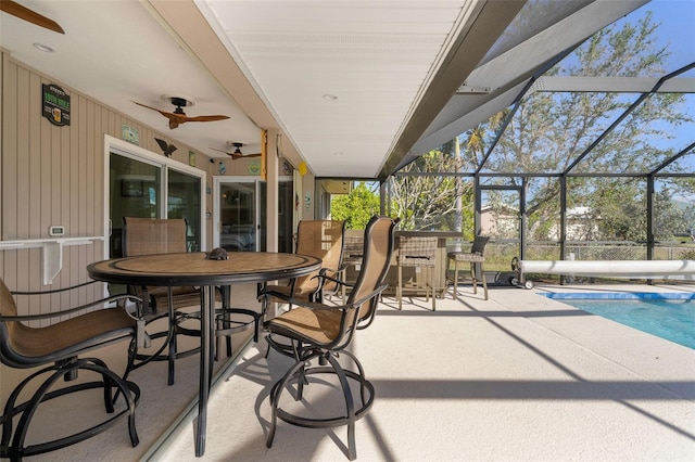 view of patio with glass enclosure, ceiling fan, and an outdoor bar