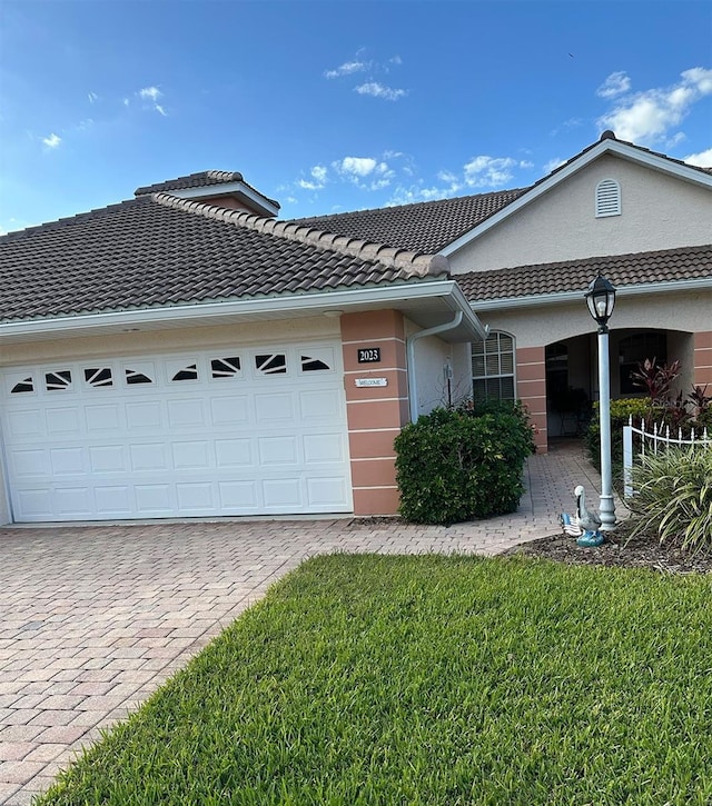 single story home featuring a garage, a tile roof, decorative driveway, a front lawn, and stucco siding