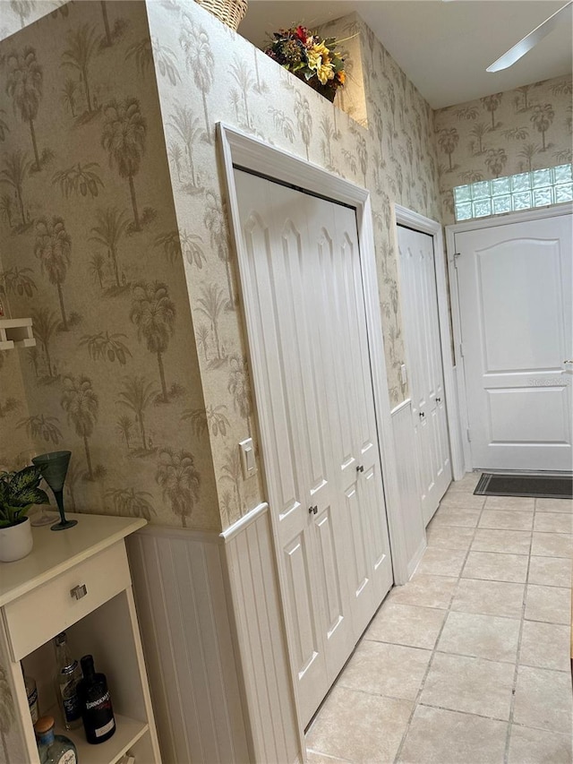 hallway featuring a wainscoted wall, light tile patterned floors, and wallpapered walls