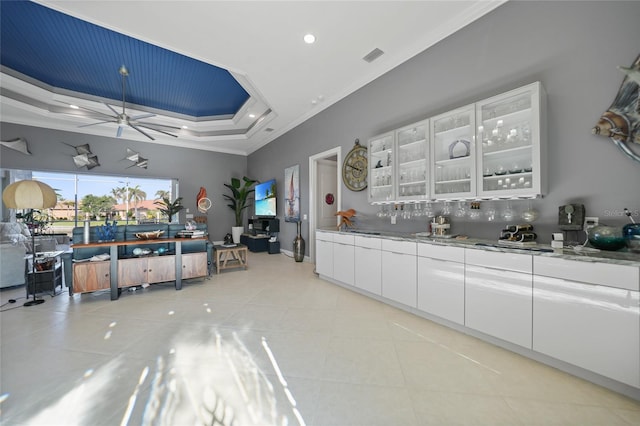 kitchen with ornamental molding, a raised ceiling, ceiling fan, light tile patterned floors, and white cabinetry