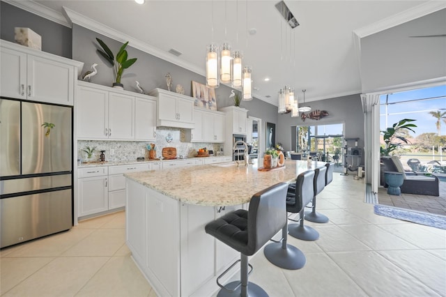 kitchen with white cabinetry, stainless steel refrigerator, a kitchen island with sink, and pendant lighting