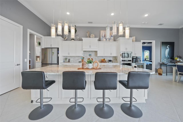 kitchen featuring white cabinets, appliances with stainless steel finishes, decorative light fixtures, and a large island with sink