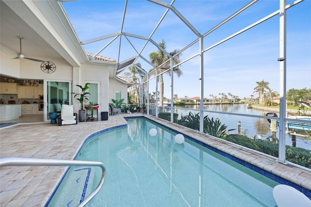 view of pool featuring glass enclosure, ceiling fan, a water view, and a patio