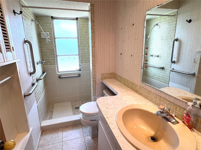 bathroom with toilet, vanity, a tile shower, and tile patterned flooring