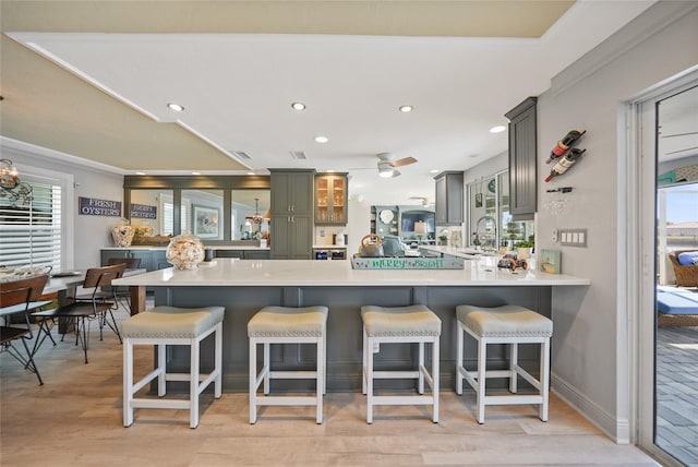 kitchen featuring gray cabinetry, ceiling fan, light hardwood / wood-style floors, kitchen peninsula, and a breakfast bar area