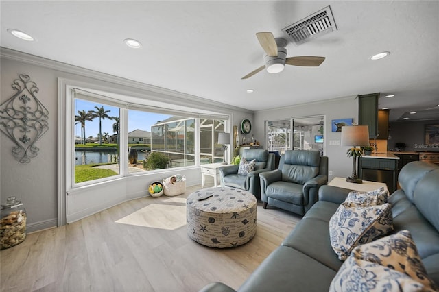 living room featuring a water view, light hardwood / wood-style flooring, ceiling fan, and crown molding