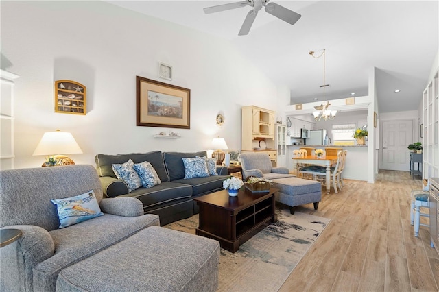 living room with ceiling fan with notable chandelier, light hardwood / wood-style floors, and high vaulted ceiling