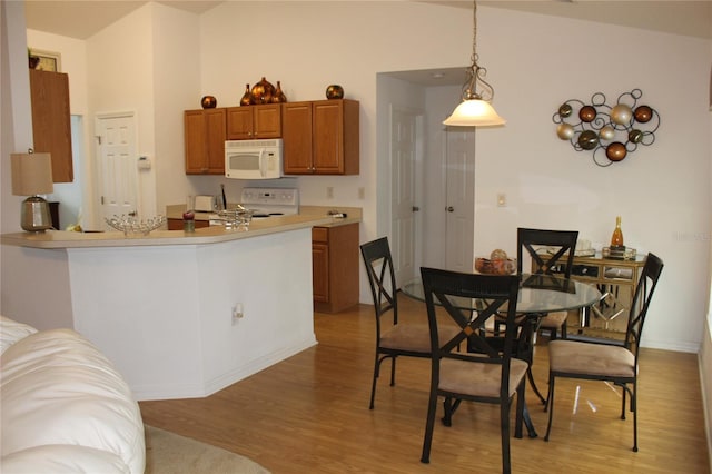 kitchen with kitchen peninsula, white appliances, hanging light fixtures, and light hardwood / wood-style flooring