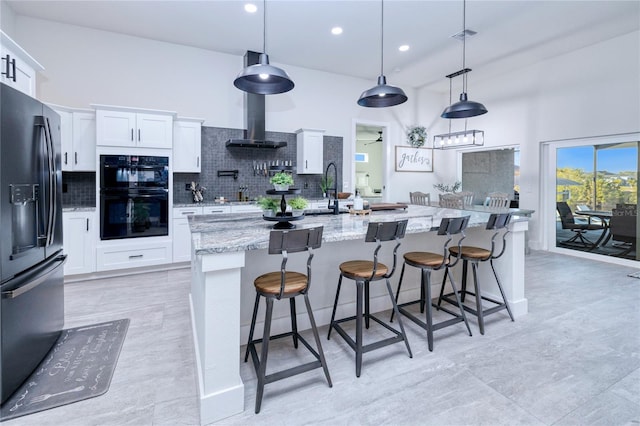 kitchen featuring white cabinetry, light stone counters, an island with sink, decorative light fixtures, and black appliances