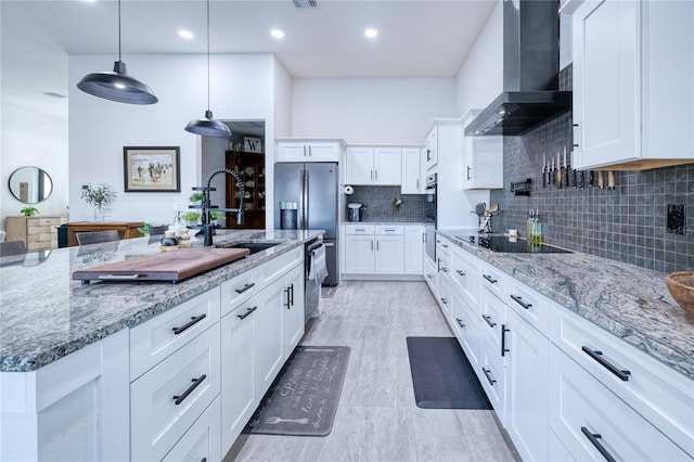 kitchen featuring white cabinetry, sink, wall chimney range hood, an island with sink, and pendant lighting