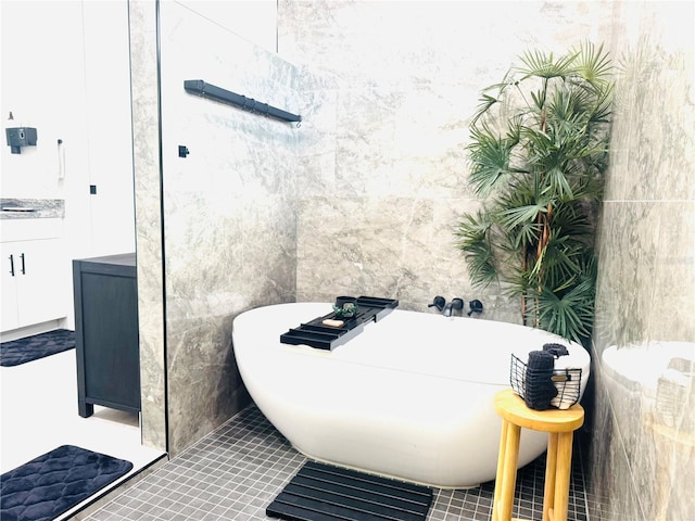 bathroom featuring tile patterned floors, a bathing tub, vanity, and tile walls