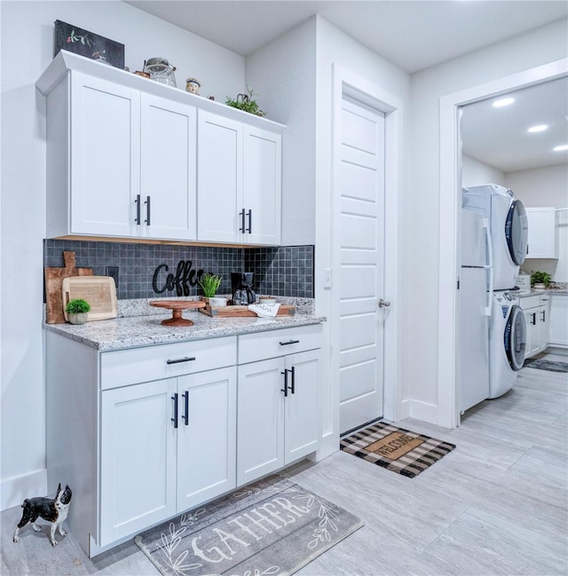 interior space featuring white cabinets, stacked washer / drying machine, light stone countertops, and backsplash