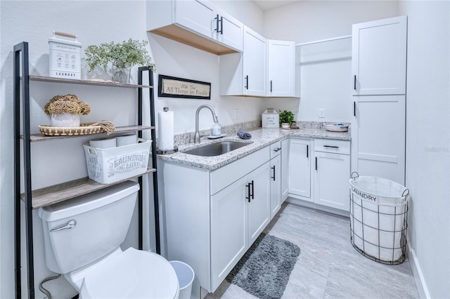 kitchen featuring white cabinets, light stone countertops, and sink