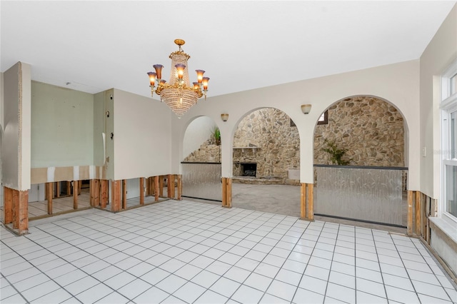 unfurnished room featuring a notable chandelier and a stone fireplace