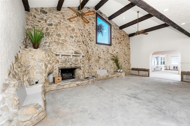 unfurnished living room featuring beamed ceiling, ceiling fan, a stone fireplace, and high vaulted ceiling