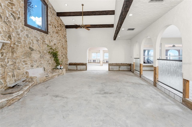 unfurnished living room with beam ceiling, ceiling fan, concrete floors, and a towering ceiling