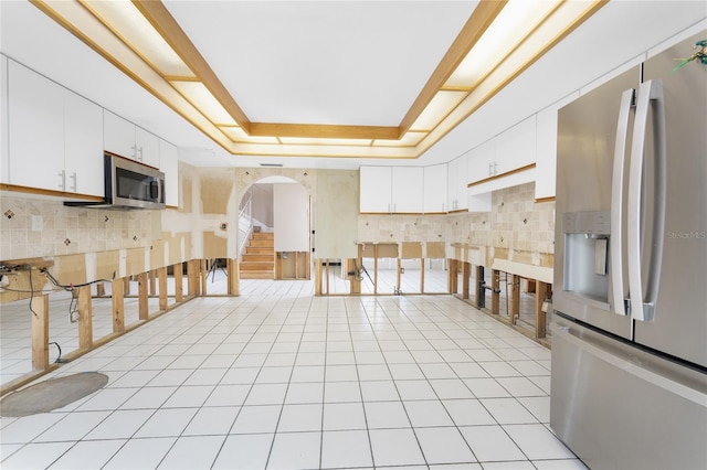 kitchen featuring a raised ceiling, white cabinets, light tile patterned floors, and appliances with stainless steel finishes