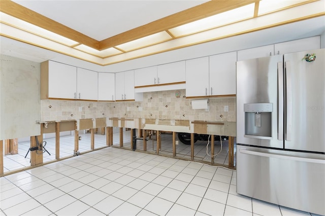 kitchen with decorative backsplash, stainless steel fridge, light tile patterned floors, and white cabinetry