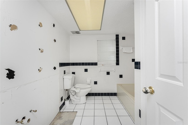 bathroom with tile patterned flooring, toilet, a textured ceiling, a tub to relax in, and tile walls