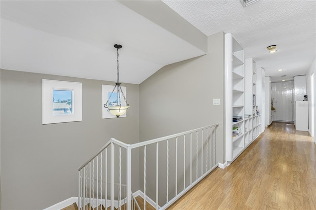 hall with hardwood / wood-style flooring, vaulted ceiling, and a textured ceiling