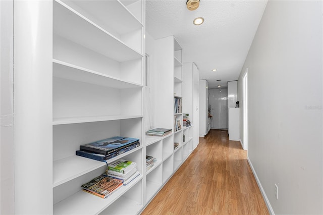 corridor with a textured ceiling and light wood-type flooring