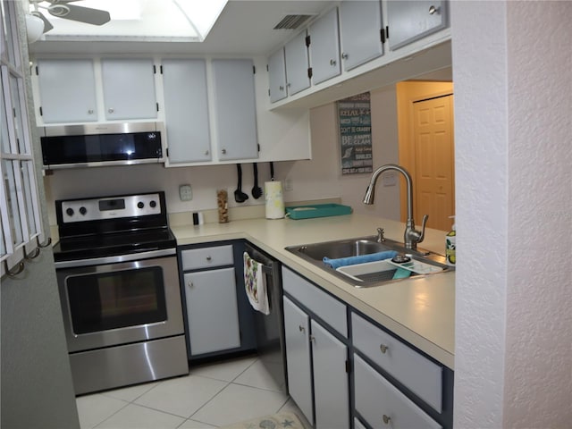 kitchen with gray cabinetry, stainless steel appliances, ceiling fan, sink, and light tile patterned flooring