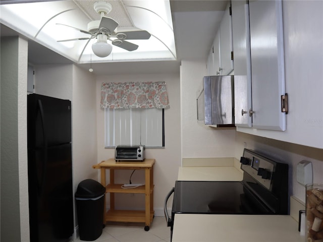 kitchen with black refrigerator, electric range oven, ceiling fan, light tile patterned floors, and white cabinetry